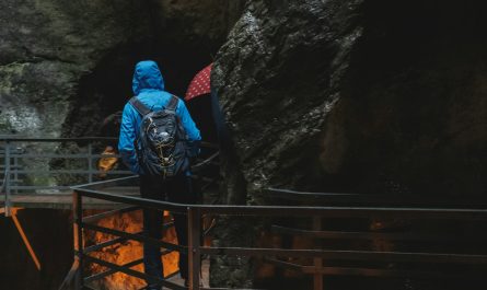 person wearing blue hooded jacket standing on footbridge near cave