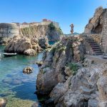 man standing on rock formation near body of water during daytime