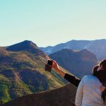 a woman taking a picture of the mountains with her cell phone