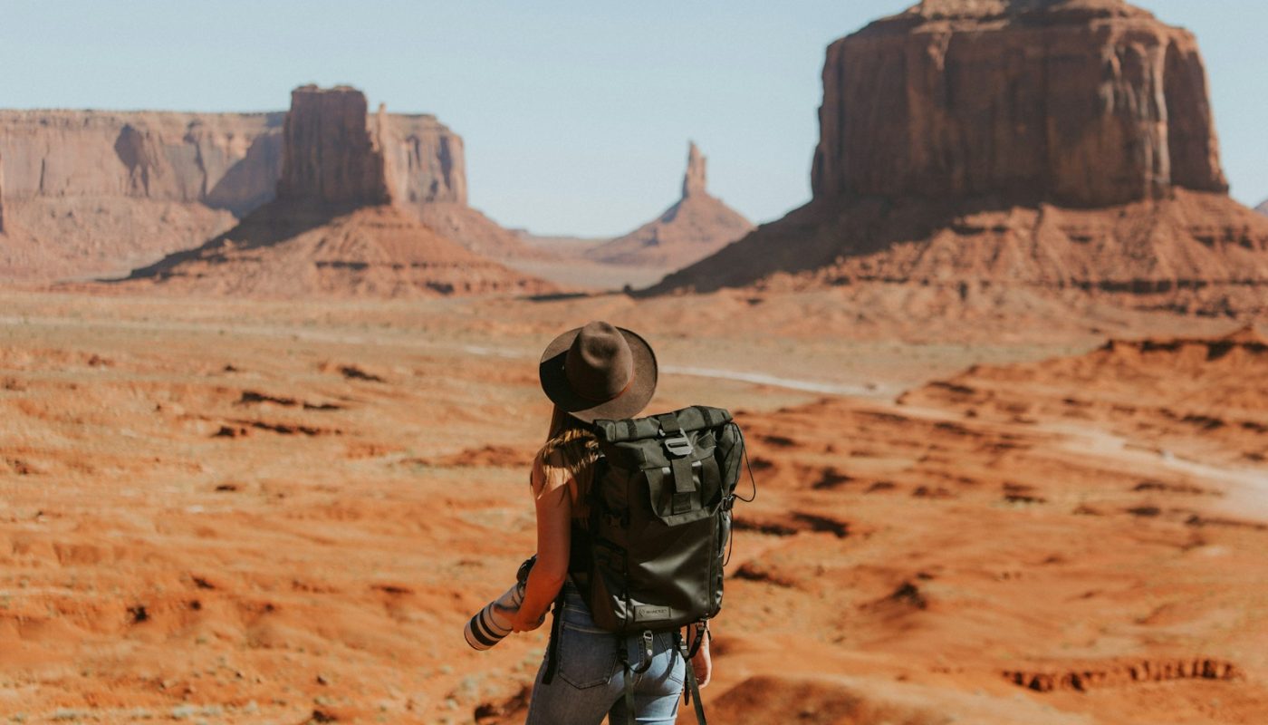 woman with black backpack standing on brown dessert