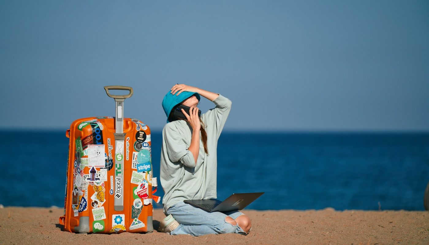 a person sitting on a beach with a suitcase and a laptop
