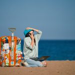 a person sitting on a beach with a suitcase and a laptop
