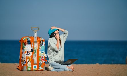 a person sitting on a beach with a suitcase and a laptop
